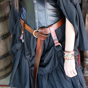 May include: A black leather corset with a brown leather belt and a silver buckle. The corset has a lace trim and is worn over a black skirt.
