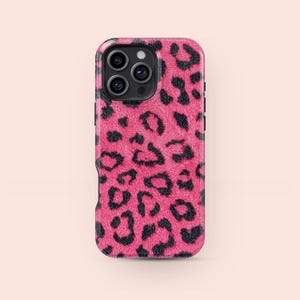 May include: A pink phone case featuring a black leopard print pattern. The case has a glossy finish and a raised edge around the camera lenses. The leopard spots are irregularly shaped and scattered across the surface.
