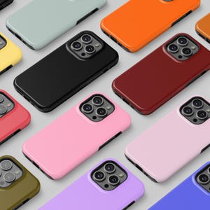 May include: A collection of colorful phone cases in various shades, including black, pink, orange, and green. The cases are arranged in a pattern, showcasing their glossy finish and camera cutouts. The cases are designed for a smartphone.