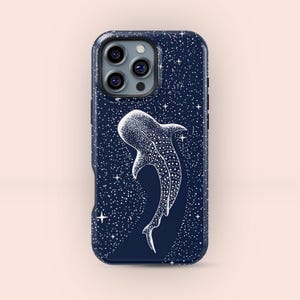 以下が含まれることがあります： 紺色の携帯電話ケース。白いジンベイザメのイラストが星空を背景に描かれています。ケースは光沢仕上げで、スマートフォンを保護するように設計されています。