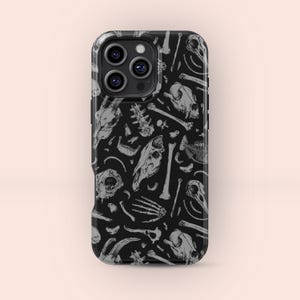 May include: Black phone case featuring a repeating pattern of gray animal skulls, bones, and skeletal elements. The case has a glossy finish and a camera module with three lenses. The design is a macabre, yet artistic, illustration.