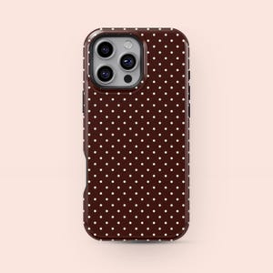May include: A brown phone case with a white polka dot pattern. The case has a glossy finish and a camera cutout. The phone case is designed to fit a smartphone.