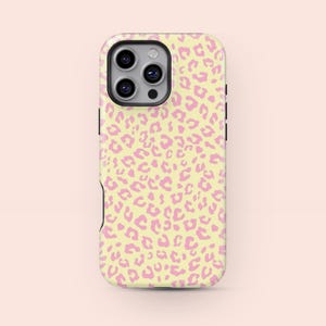 May include: A phone case with a light yellow background and a pink leopard print pattern. The case has a black camera module and black side buttons. The case is designed to fit a smartphone.