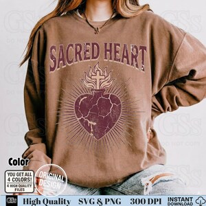 Op de afbeelding: Bruin sweatshirt met de tekst "SACRED HEART" boven een hartontwerp met een kruis en vlammen. Het hart heeft een distressed, vintage look. Het sweatshirt heeft ook de tekst "Color", "Original Design", "High Quality SVG & PNG" en "Instant Download".