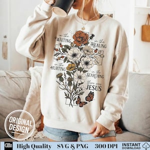 May include: Cream-colored sweatshirt with a floral cross design. The cross is composed of white, orange, and yellow flowers, with butterflies and the text "in the WAITING, in the HEALING, in the HURTING, in the SEARCHING, there was JESUS".