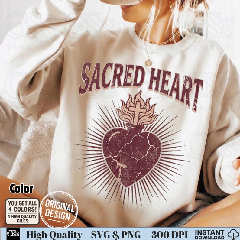 Op de afbeelding: Cr&egrave;mekleurige sweatshirt met de tekst "SACRED HEART" in een verweerde, bordeauxrode letter. Daaronder een bordeauxrood hartontwerp met een kruis en vlammen, omringd door stralende lijnen.