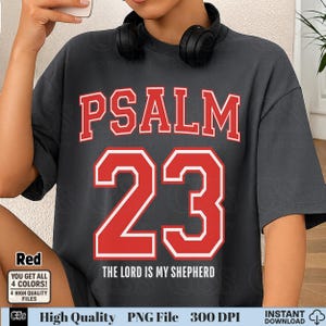 Könnte beinhalten: Dunkelgraues T-Shirt mit dem Text "PSALM 23" in roten Blockbuchstaben. Unter der Zahl 23 steht der Text "THE LORD IS MY SHEPHERD" in Weiß. Das Shirt hat einen Rundhalsausschnitt und kurze Ärmel.