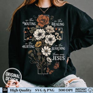 May include: Black sweatshirt featuring a floral cross design with the words "in the WAITING, in the HEALING, in the HURTING, in the SEARCHING, there was JESUS." The design includes flowers and butterflies. "ORIGINAL DESIGN" is also printed on the sweatshirt.