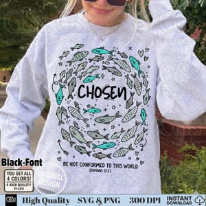 May include: A light gray sweatshirt with a fish design in a circle around the word "CHOSEN". The design includes teal and gray fish, hearts, and stars. The text "BE NOT CONFORMED TO THIS WORLD (ROMANS 12:2)" is also printed on the sweatshirt.