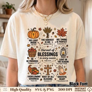 May include: A cream-colored t-shirt featuring a graphic print with autumn-themed illustrations including a pumpkin, wheat, maple leaf, lantern, cornucopia, and praying hands, accompanied by the text Harvest of Blessings in every season.