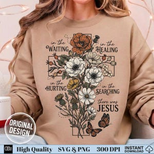 May include: A tan sweatshirt featuring a floral cross design with the words "in the Waiting, in the Healing, in the Hurting, in the Searching, there was JESUS." The design includes flowers and butterflies.