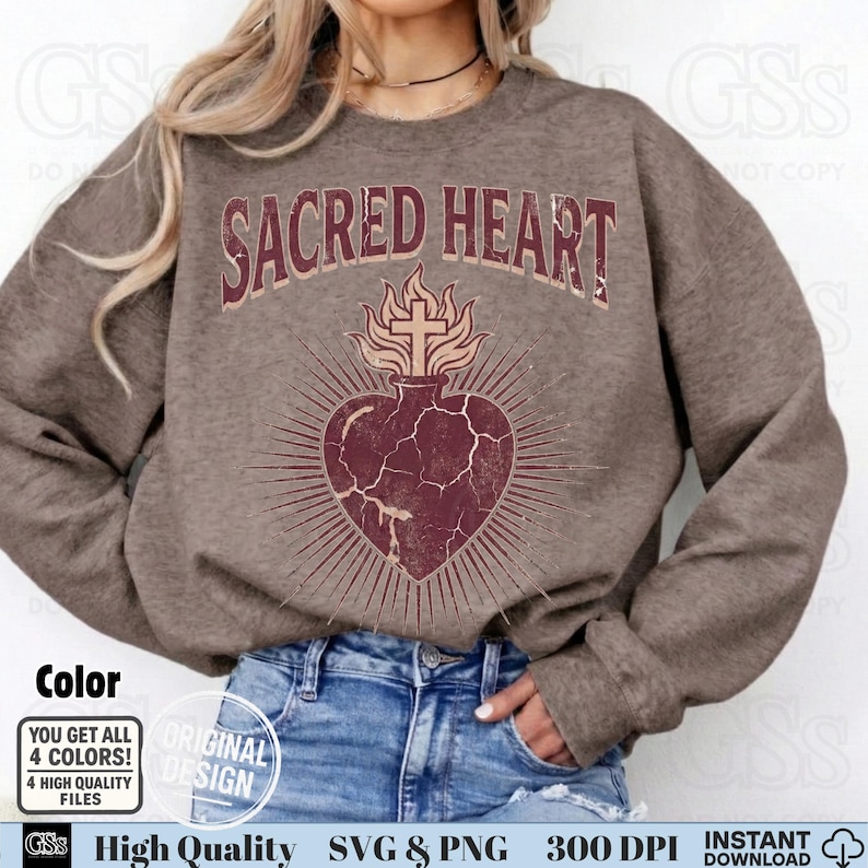 Op de afbeelding: Een bruine sweatshirt met de tekst "SACRED HEART" boven een hartontwerp met een kruis en vlammen. Het hart is dieprood met stralende lijnen. De sweatshirt heeft een neutrale kleur, geschikt voor diverse stijlen.