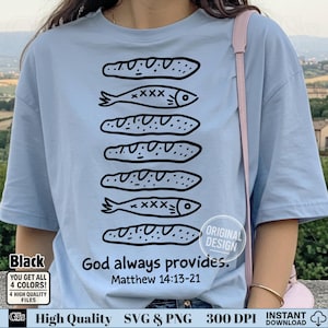 Puede incluir: Camiseta azul claro con un diseño negro de panes y peces. El texto "God always provides. Matthew 14:13-21" está impreso debajo del diseño. La camiseta también tiene un pequeño gráfico en blanco y negro en la esquina inferior izquierda.