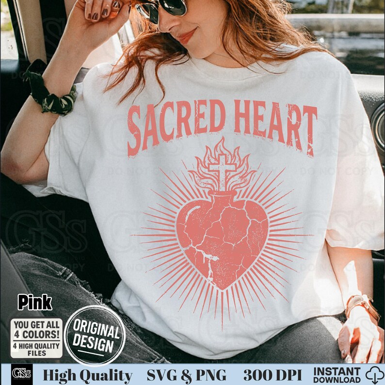 Op de afbeelding: Wit T-shirt met een roze grafisch ontwerp. Het ontwerp toont de woorden "SACRED HEART" boven een hart met een kruis en stralende lijnen, met een verweerde, vintage look. Extra tekst bevat "Pink", "Original Design" en "High Quality SVG & PNG".
