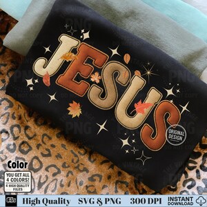 May include: Black t-shirt with the word "JESUS" in a fall-themed design. The letters are in shades of brown and beige, with autumn leaves and starburst accents. The shirt also has the text "ORIGINAL DESIGN".