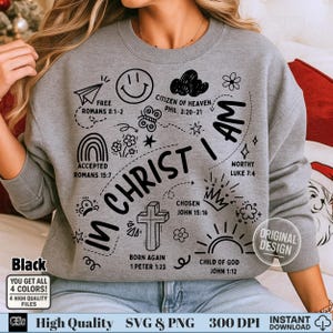 Puede incluir: Sudadera gris con la frase "IN CHRIST I AM" y varias ilustraciones de garabatos, incluyendo una cruz, un arcoíris y una carita sonriente. La sudadera también tiene el texto "Black" y "YOU GET ALL 4 COLORS!"