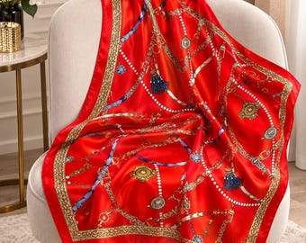 May include: A square silk scarf in a vibrant red hue featuring a detailed gold chain and belt print. The design includes intricate patterns of white pearls, blue tassels, and ornate circular medallions arranged in a classic, repeating motif.