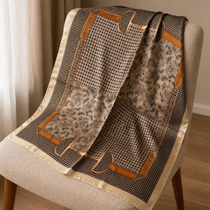 Peut inclure: Un foulard carré présentant un mélange de motifs pied-de-poule noir et blanc et de sections cachemire beiges. Le design est rehaussé de lanières couleur cuir fauve et de motifs de mors dorés, avec une bordure unie couleur crème.