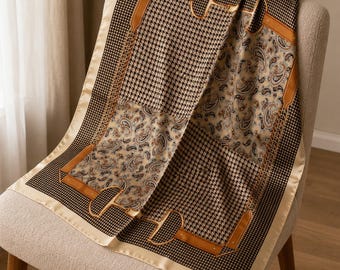 May include: A square scarf featuring a mix of black and white houndstooth patterns and beige paisley sections. The design is accented with tan leather-colored straps and gold-toned horse bit hardware motifs, finished with a solid cream border.