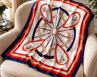 May include: A square silk scarf featuring a white center with a navy blue and red border. The design includes a central wheel motif with radiating spokes, surrounded by four red shield-shaped emblems and tan belt-like straps with gold buckles.