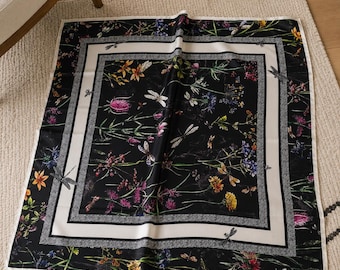May include: Square black scarf with a floral and dragonfly pattern. The scarf features a white border with a gray and black patterned trim. The scarf is decorated with colorful flowers and dragonflies.