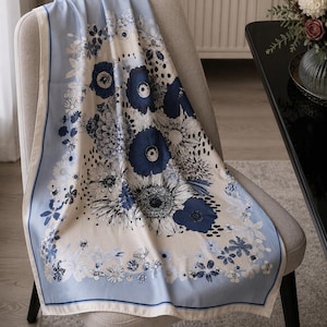 Op de afbeelding: Een vierkante sjaal met een crèmekleurig midden en een dicht bloemenpatroon in tinten donkerblauw, marineblauw en zwart. Het ontwerp is omlijst door een effen lichtblauwe rand met een dunne donkerblauwe lijn voor een duidelijk contrast.