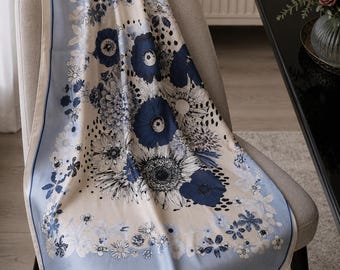 May include: A square scarf featuring a cream-colored center with a dense floral pattern in shades of dark blue, navy, and black. The design is framed by a solid light blue border with a thin dark blue line, creating a distinct contrast.