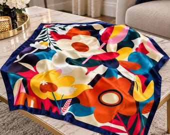 May include: A square silk scarf featuring a vibrant floral pattern with large stylized flowers in shades of orange, yellow, red, and cream, set against a deep navy blue background with a solid navy blue border along the edges.