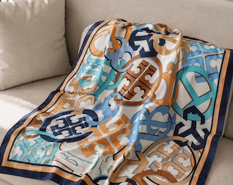 May include: A square silk scarf with a repeating pattern of interlocking geometric shapes in shades of blue, orange, and brown on a white background. The scarf has a navy blue border with an orange accent.