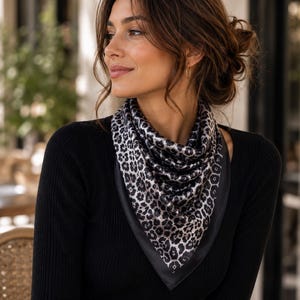 May include: A black long-sleeve top paired with a leopard print scarf. The scarf features a black border and a pattern of black and gray spots. The woman is wearing gold hoop earrings.