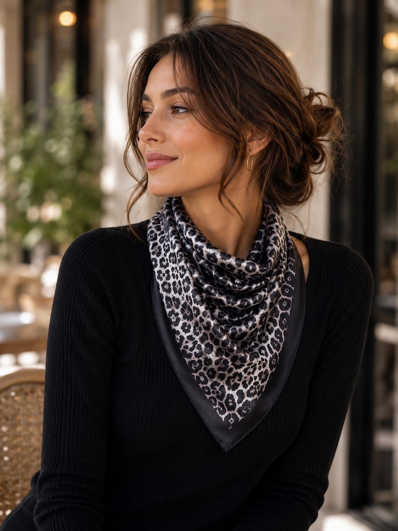 May include: A black long-sleeve top paired with a leopard print scarf. The scarf features a black border and a pattern of black and gray spots. The woman is wearing gold hoop earrings.