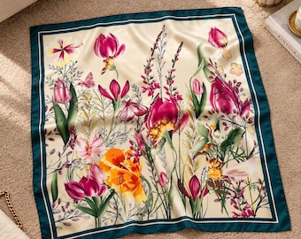 May include: A square silk scarf featuring a cream-colored background with a vibrant botanical print of pink, orange, and yellow tulips and wildflowers. The scarf is framed by a solid dark teal border and thin white lines along the edges.