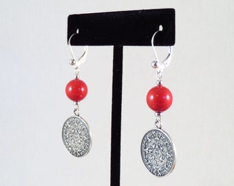 May include: Silver earrings with red beads and a silver Aztec calendar pendant.