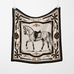 May include: Square silk scarf featuring a white horse with a black saddle. The scarf has a black border with gold accents and equestrian designs, including horseshoes and riding gear. The scarf is hanging from a clip.