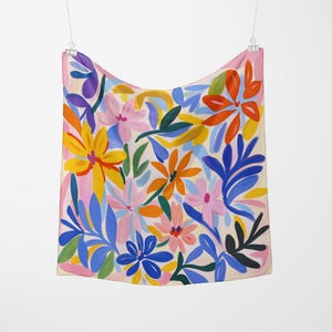May include: A square scarf with a vibrant floral pattern. The design features colorful flowers in shades of yellow, orange, pink, and blue, set against a cream background. The scarf is hanging from a metal clip.