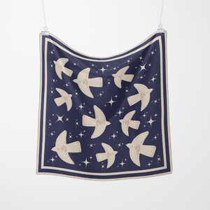 May include: A navy blue square scarf with a cream border, decorated with cream-coloured birds and white stars. The scarf is suspended from a metal clip. The design is symmetrical.