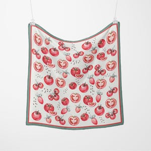 May include: A white scarf with a repeating watercolor pattern of red tomatoes and tomato slices. The scarf has a green border and is hanging from a silver clip.
