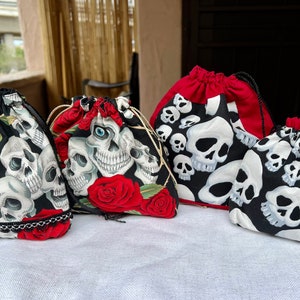 Pode incluir: Quatro sacos de cordão com desenhos de caveiras e rosas. Os sacos são feitos de tecido preto com caveiras brancas e rosas vermelhas. Os sacos são de tamanhos diferentes e têm desenhos diferentes.