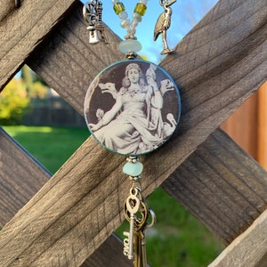 May include: A white beaded necklace with a silver charm of a crane, a silver charm of a spinning wheel, and a round pendant with a black and white image of a woman with a crown. The pendant is attached to a silver chain with a key charm that says "LOVE".