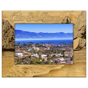 May include: Wooden picture frame with the words "Cabo San Lucas" etched across the top. The frame surrounds a scenic view of a coastal town with blue water and mountains in the background.