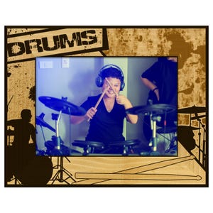 May include: A wooden picture frame with the word "DRUMS" in a distressed font. The frame holds a photo of a person playing a drum set, wearing headphones and holding drumsticks. The frame has a light wood grain.