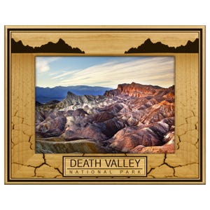 May include: A wooden picture frame featuring a landscape photograph of Death Valley National Park. The frame has a light brown finish with a dark brown border and mountain silhouettes at the top. The text "DEATH VALLEY NATIONAL PARK" is displayed at the bottom.