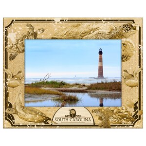 May include: A rectangular photo frame with a scenic image of a lighthouse on the coast. The frame is tan with etched sea turtles and the words "SOUTH CAROLINA". The image shows a lighthouse, marsh, and blue sky.