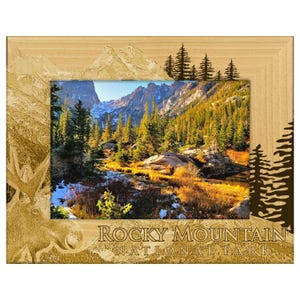 May include: Wooden picture frame with a scenic view of the Rocky Mountain National Park. The frame is light brown with etched mountain and tree designs. The text "Rocky Mountain National Park" is at the bottom.