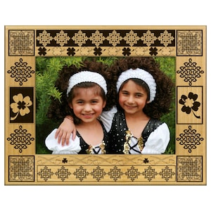 May include: Wooden picture frame with Celtic knot and shamrock designs. The frame surrounds a photo of two young girls in Irish dance attire, wearing white headbands and black and white dresses.