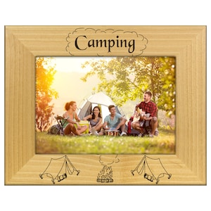 May include: Wooden picture frame with a camping theme. The frame features the word "Camping" at the top and camping-related illustrations. The photo inside shows a group of people camping near a tent, with a campfire and a person playing a guitar.