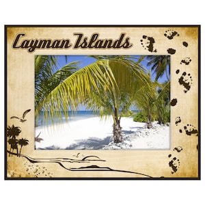 May include: A framed print featuring a tropical beach scene with palm trees, white sand, and blue water. The frame is tan with the words "Cayman Islands" at the top. Decorative elements include footprints and silhouettes of birds and palm trees.