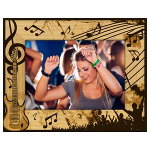 May include: Wooden picture frame with a musical theme. The frame features a guitar, musical notes, and a treble clef design. The frame surrounds a photo of people dancing at a concert. The frame is rectangular and has a light brown finish.