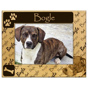 May include: Wooden picture frame featuring a dog named Bogle. The frame has a brown and white dog image, paw prints, and a bone icon. The frame is light brown with the name "Bogle" repeated.