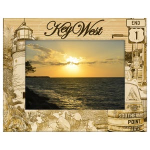 May include: Wooden picture frame featuring a sunset over the ocean. The frame is etched with a lighthouse, palm trees, and the words "Key West." Includes the "End 1" sign and the Southernmost Point marker.